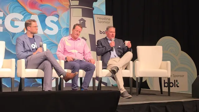 Three panelists seated on white chairs on the ITC Vegas stage, one speaking into a microphone, with bolt headline sponsor signage behind them.