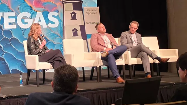 A moderator speaking into a microphone and two panelists seated on white chairs on the ITC Vegas stage, with ServiceNow headline sponsor signage behind them.